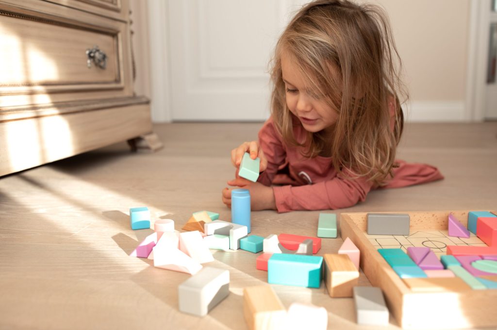 Child girl builds tower of wooden pastel colorful cubes. Children development, educational games